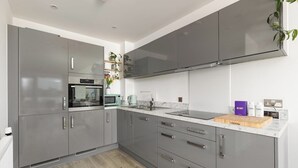 Een moderne keuken met grijze kastjes, een magnetron, een koffiezetapparaat en een houten snijplank.