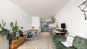 Een moderne woonkamer met een groene bank, een houten salontafel en een eethoek met een houten tafel en stoelen.