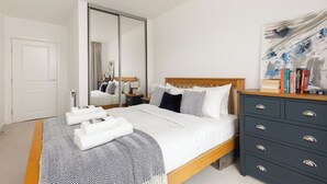 Een slaapkamer met een bed, een kaptafel, een spiegel en een schilderij aan de muur.