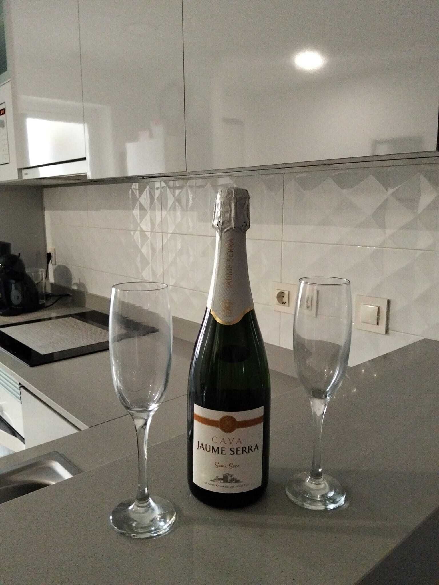 A bottle of Jaume Serra cava wine on a kitchen counter with two empty wine glasses.