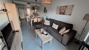A modern living room with a sofa, coffee table, TV, and a dining area in the background. - Cocoon Andalou, a little paradise with two pools in Andalusia (AN)