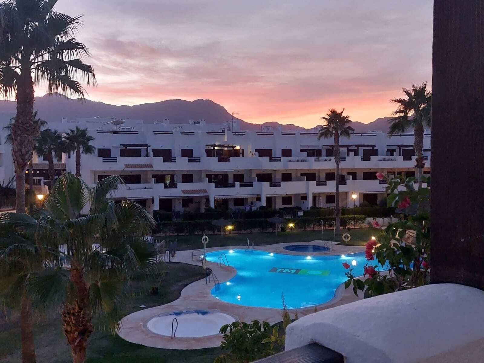 A resort with a swimming pool, palm trees, and a building with multiple balconies.