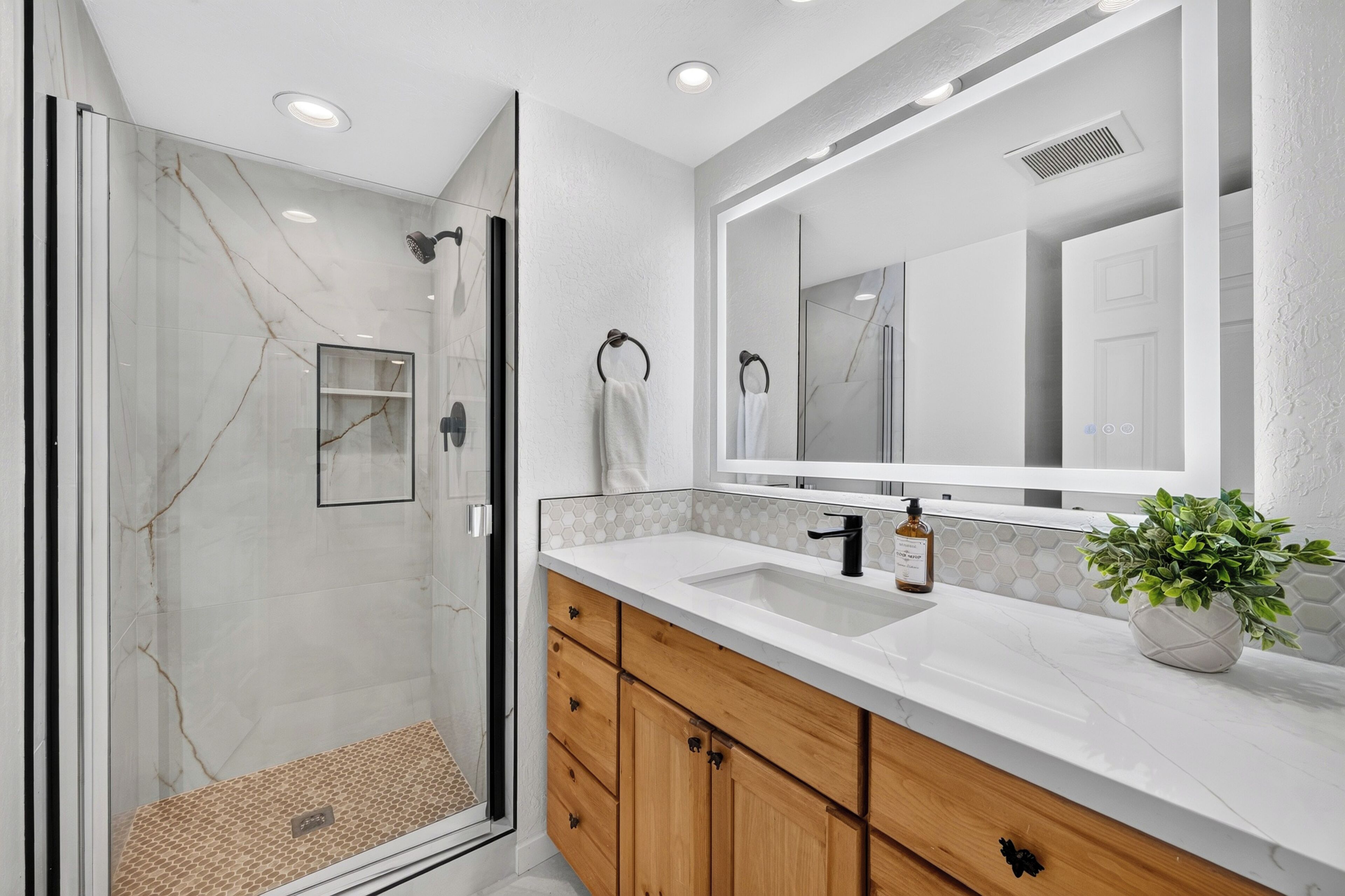 A modern bathroom with a glass shower enclosure, a large mirror, and wooden cabinets.