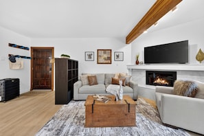 A living room with a sofa, a coffee table, a fireplace, a television, and a door. - Walk to Lifts + Tram and KT-22 Views | Olympic Valley | Tram Condo (Olympic Valley)