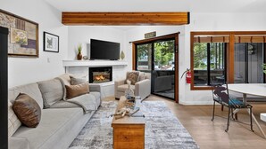 A modern living room with a fireplace, sofa, coffee table, and a dining area with a table and chairs. - Walk to Lifts + Tram and KT-22 Views | Olympic Valley | Tram Condo (Olympic Valley)