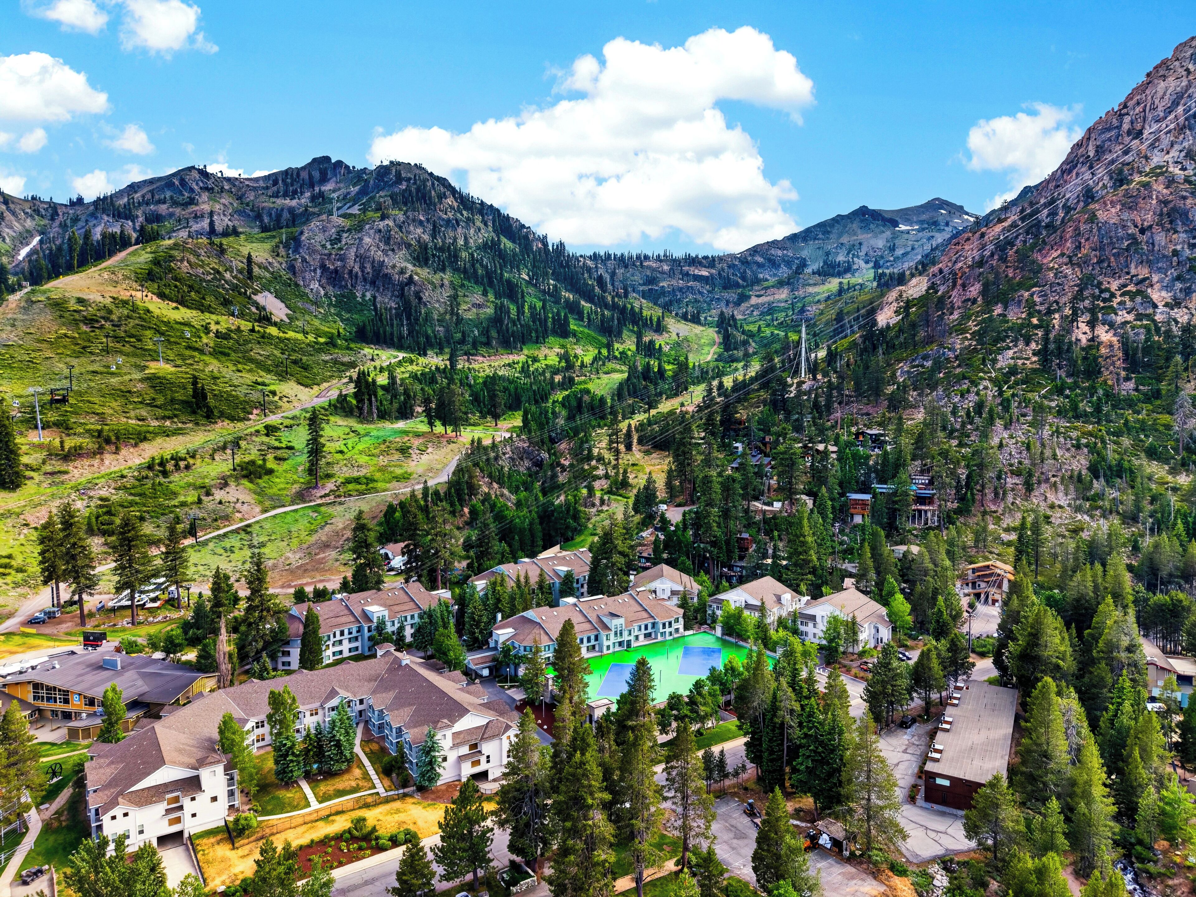 A residential area with houses, a green sports field, and mountains in the background.