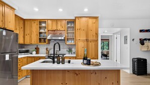 A modern kitchen with wooden cabinets, a stainless steel refrigerator, a microwave, and a large island with a sink. - Walk to Lifts + Tram and KT-22 Views | Olympic Valley | Tram Condo (Olympic Valley)