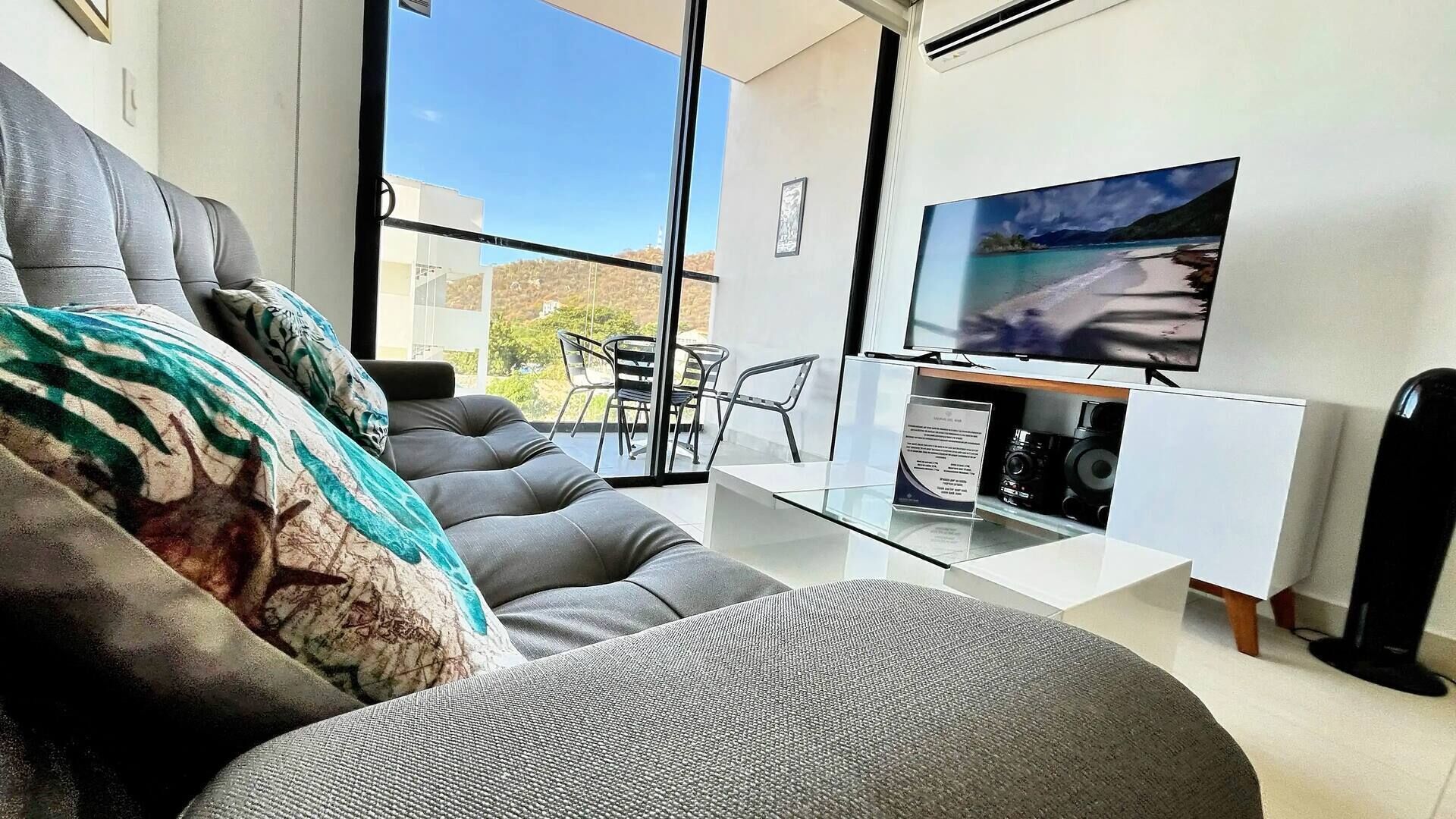 Een moderne woonkamer met een grijze bank, een glazen salontafel en een flatscreen televisie.