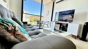En moderne stue med en grå sofa, et glasbord og et fladskærms-TV.