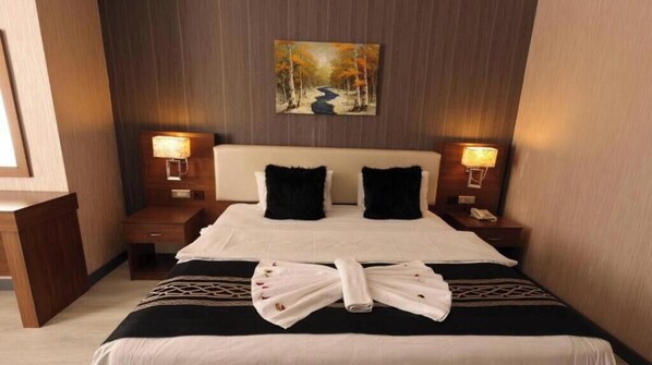 A hotel room with a bed, two bedside tables, a headboard, and a painting on the wall. - Royal Berk Hotel (VAN)