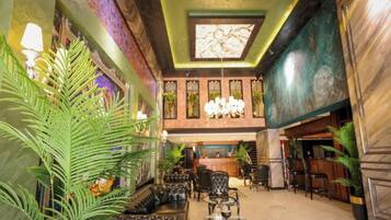 A lobby with a high ceiling, a chandelier, seating area, and potted plants.