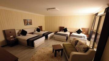 Quarto de hotel com duas camas, um sofá, uma mesa pequena e uma janela.