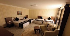 A hotel room with four beds, a sofa, a small table, and a large window. - Royal Berk Hotel (VAN)