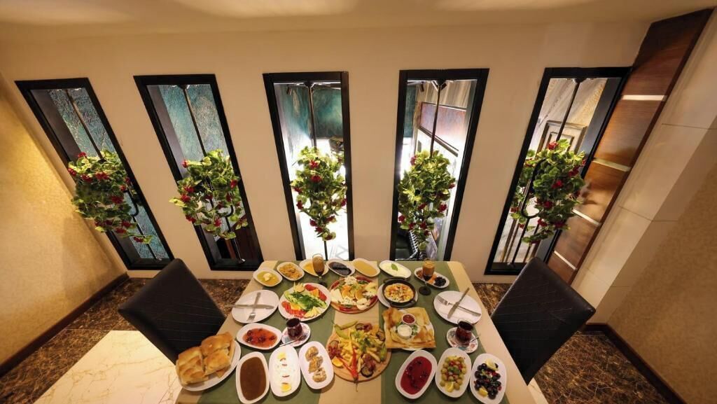 A dining table with various dishes, surrounded by chairs, in a room with large windows and potted plants.