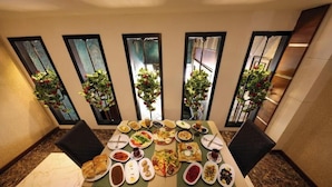 Comedor con una mesa dispuesta para una comida, rodeado de grandes ventanales con plantas.