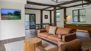 A living room with a brown leather sofa, a pool table, a television, and a wooden coffee table. - Highwoods Cottage - Authentic charm in the heart of Wine Country (Pokolbin)