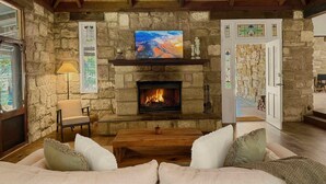 A cozy living room with a stone fireplace, a sofa, and a ceiling fan. - Highwoods Cottage - Authentic charm in the heart of Wine Country (Pokolbin)