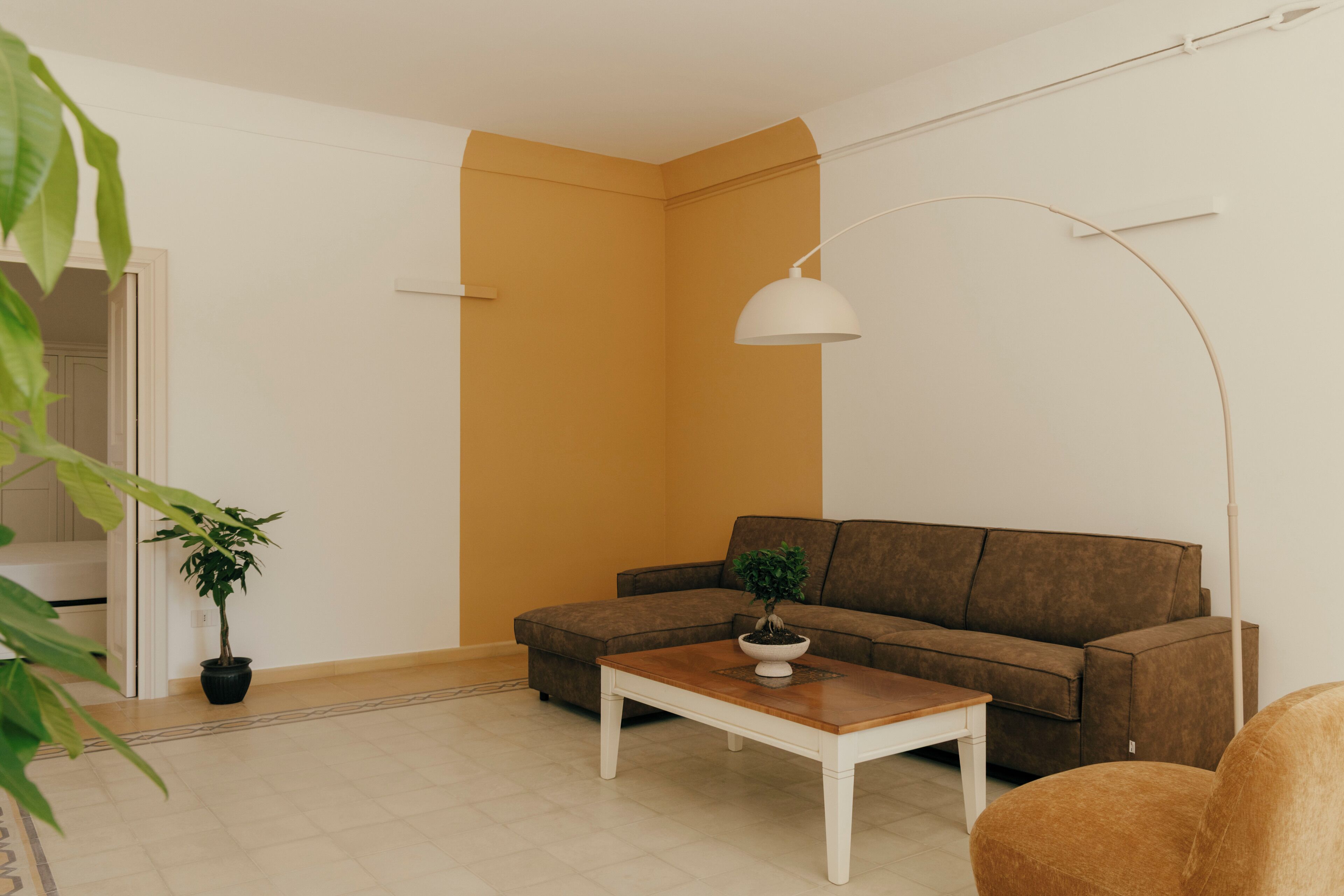 Una sala de estar con un sofá marrón, una mesa de centro blanca, una planta en maceta y una lámpara de pie.