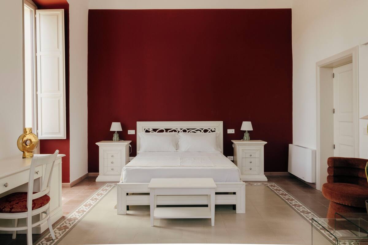 Un dormitorio con una cama grande, dos mesitas de noche, una silla, un escritorio y un ventanal.