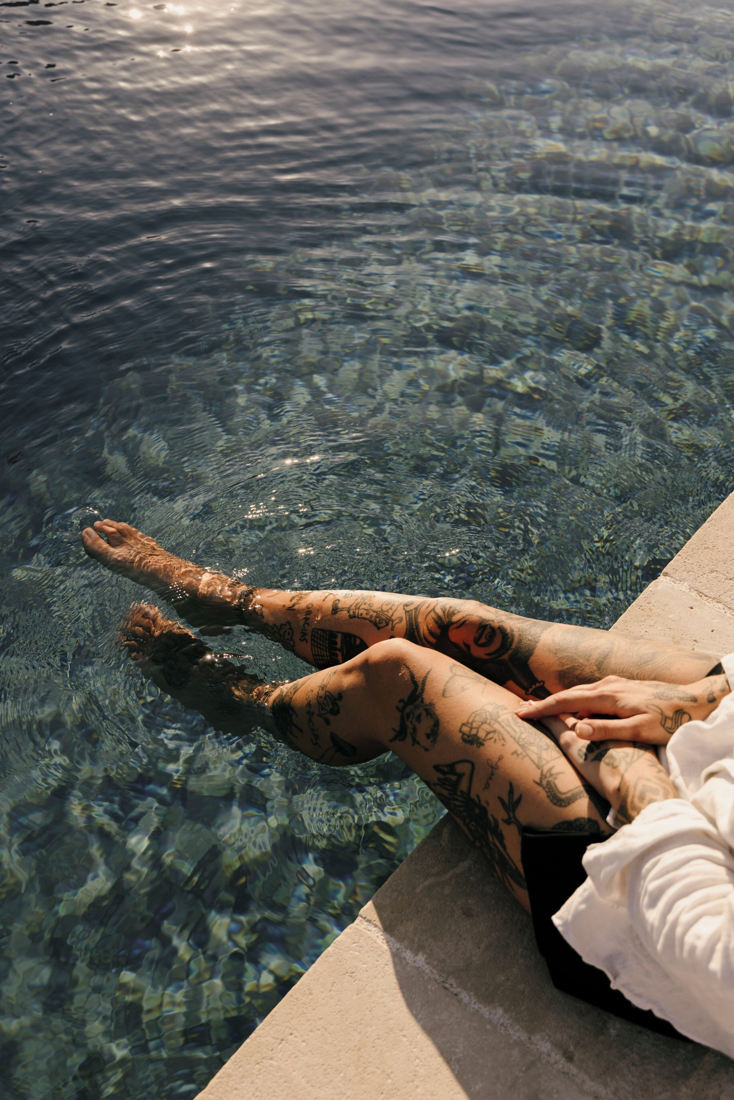 Una persona recostada en una piscina transparente mostrando tatuajes en las piernas.