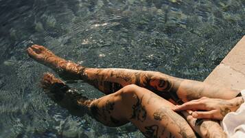Una persona recostada en una piscina transparente mostrando tatuajes en las piernas.