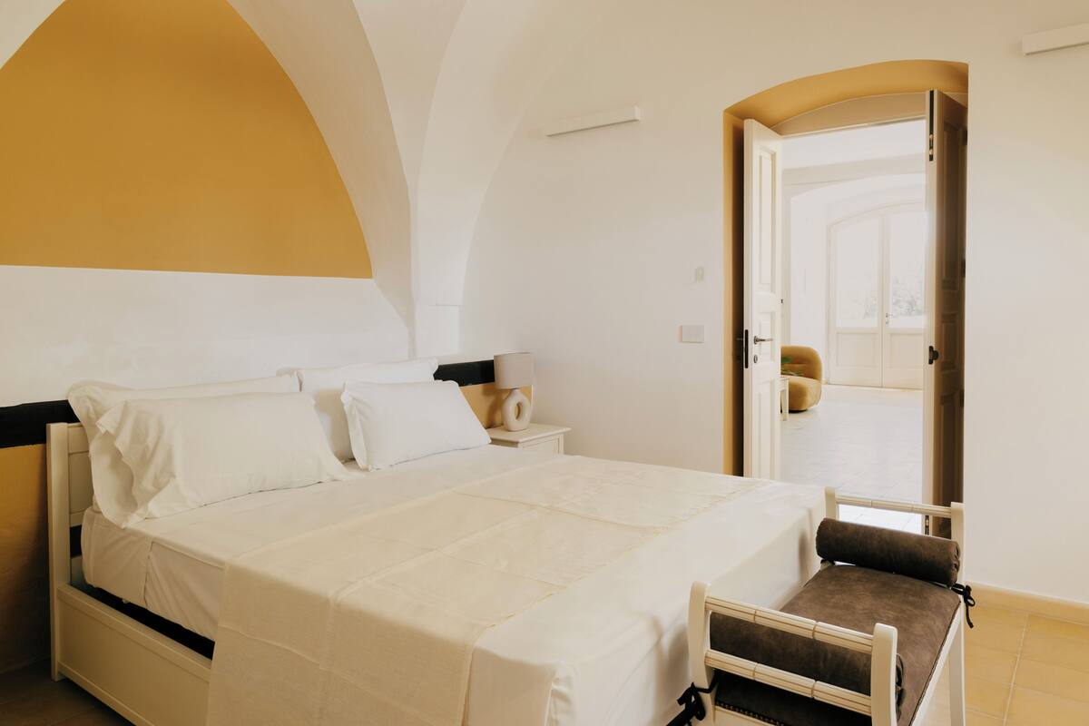 Un dormitorio con cama, mesita de noche y puerta que da a otra habitación.