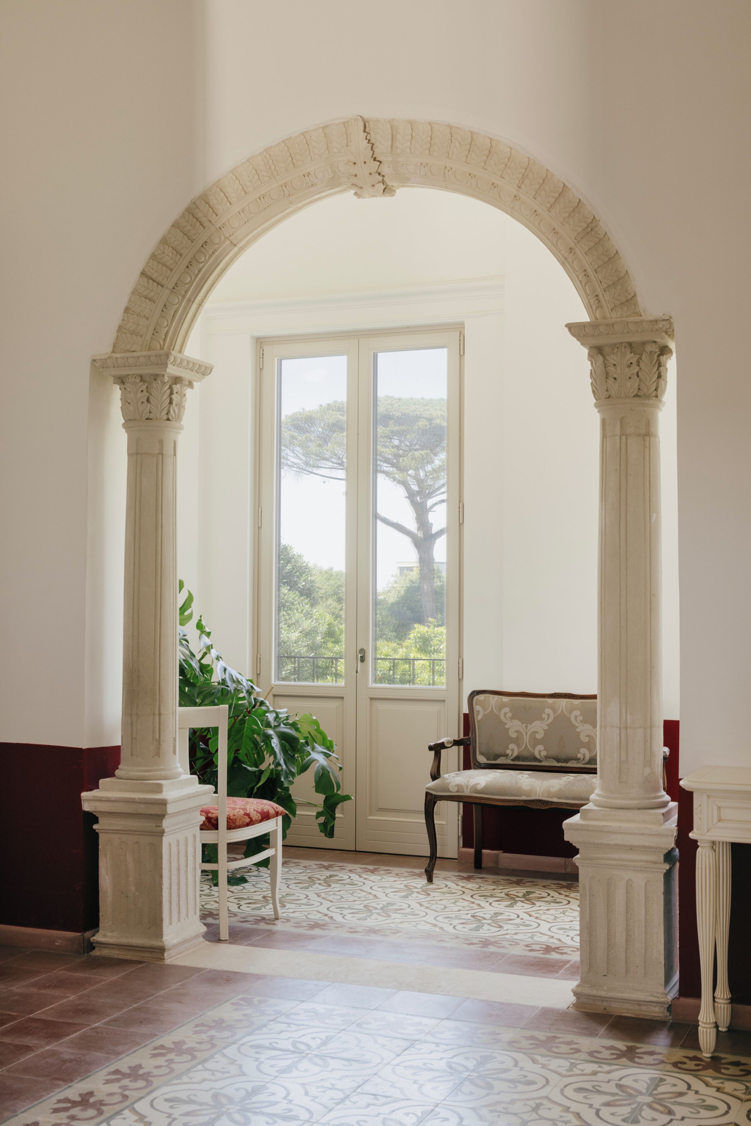 Una habitación con un amplio arco de entrada, una silla, una mesa y vistas al exterior con vegetación.