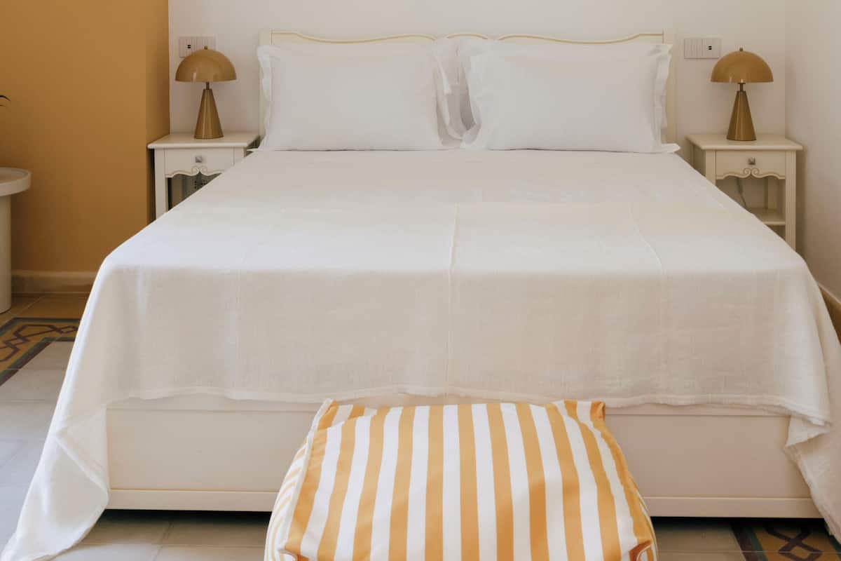 Un dormitorio con una cama, dos mesitas de noche, una lámpara en cada una y un cojín a rayas en el suelo.