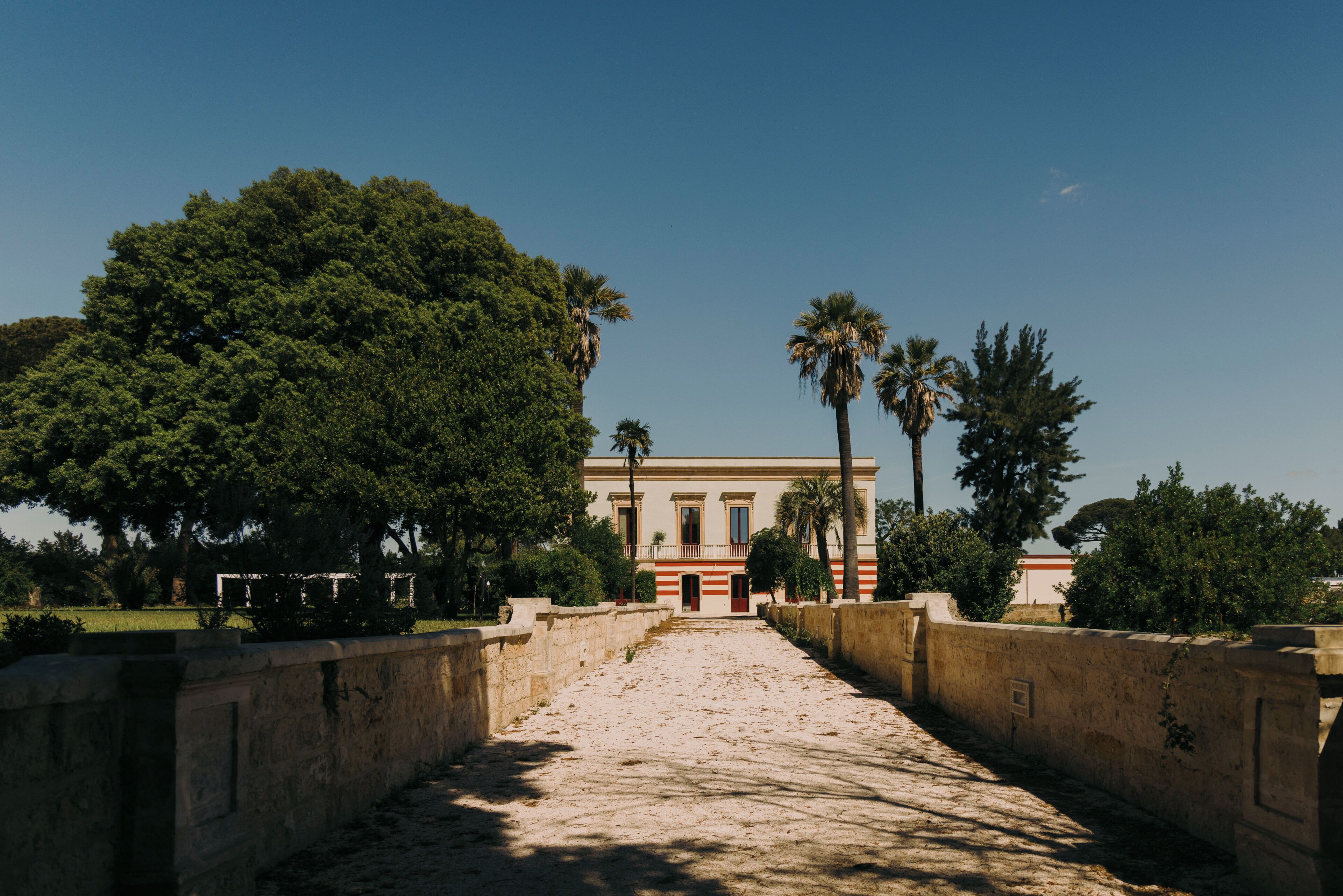 A pathway leading to a building with columns, surrounded by trees and a clear sky.