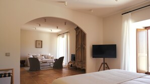 A hotel room with a bed, a TV on a stand, a sofa, and a wooden wardrobe. - Palacio de Paradinas (Santa Maria la Real de Nieva)