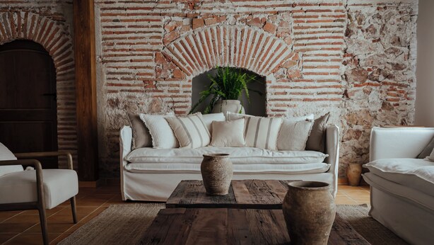 A room with a brick wall, a white sofa, a wooden coffee table, and a potted plant. - Palacio de Paradinas (Santa Maria la Real de Nieva)