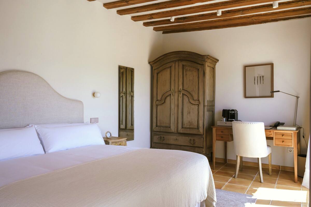 Une chambre à coucher avec un lit, une armoire en bois, un bureau avec une chaise et une lampe.