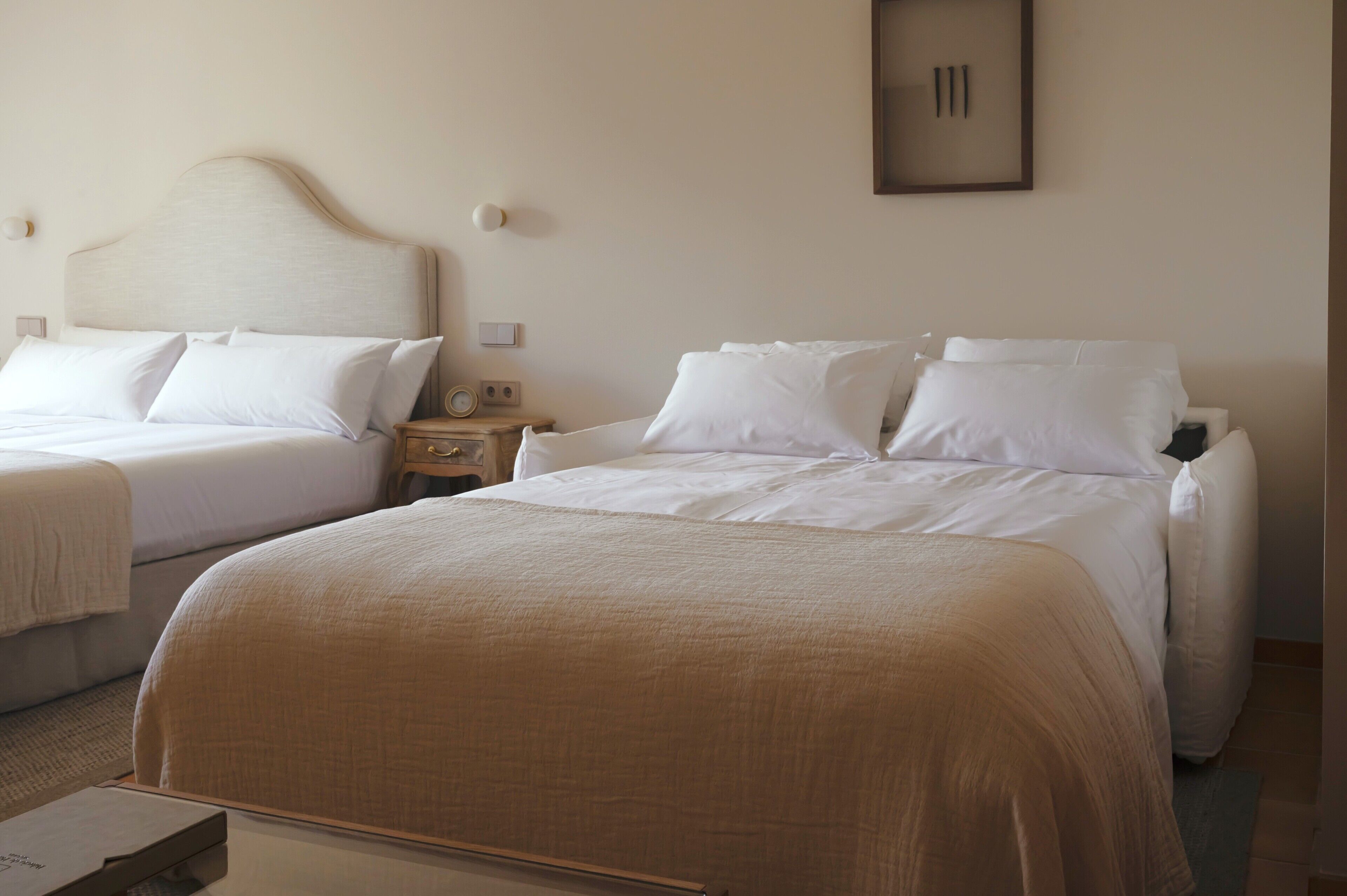 A hotel room with two beds, a bedside table with a radio, and a framed picture on the wall.