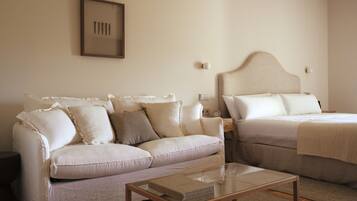 A room with a beige sofa, a bed with a headboard, a bedside table, and a framed picture on the wall.