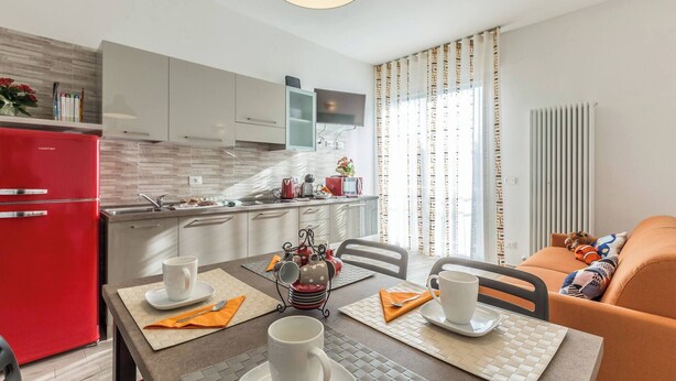 A modern kitchen with a red refrigerator, a dining table with white cups and saucers, and a sofa with colorful pillows. - Martina (Bologna)