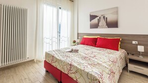 A hotel room with a bed, a bedside table, a lamp, a window with curtains, a radiator, and a wall-mounted picture. - Martina (Bologna)