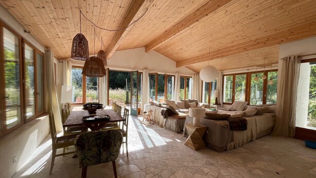 Um quarto amplo com teto de madeira alto, janelas grandes, área de refeições e um espaço de estar aconchegante.