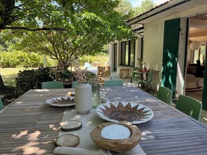Ein Essbereich im Freien mit einem Tisch für zwei, umgeben von Stühlen, und Blick auf ein Haus mit überdachter Terrasse.