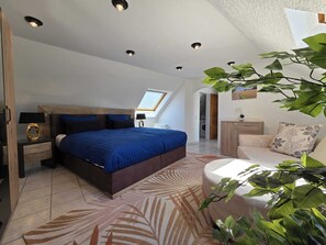 Une chambre avec un grand lit, une lucarne, un canapé et une plante.