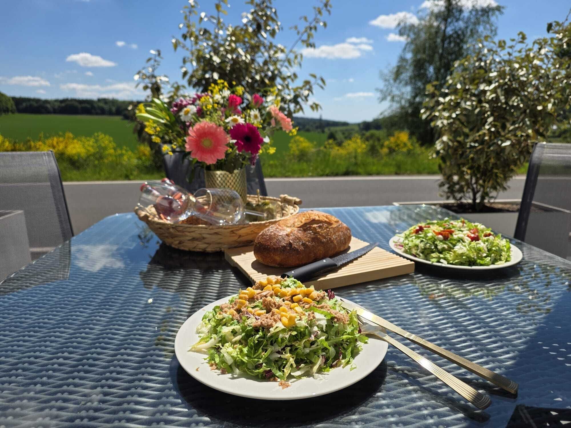 Ein Tisch mit einem Korb, einem Brotlaib, einer Salatschüssel und einer Gemüsequelle.