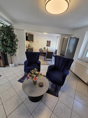 Un salon moderne avec deux fauteuils bleu foncé, une table basse ronde agrémentée d’un arrangement floral et une grande plante en pot.