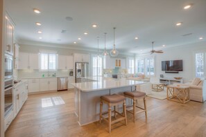 A spacious kitchen with white cabinetry, a central island with stools, and a ceiling fan. - Coconut Cove by AvantStay | Deck w/ Hot Tub, Access to 2 Pools (Santa Rosa Beach)