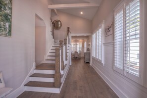 A staircase with wooden steps and white walls, leading to a dining area with a chandelier. - Coconut Cove by AvantStay | Deck w/ Hot Tub, Access to 2 Pools (Santa Rosa Beach)