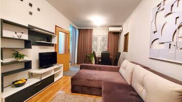 Un salon moderne avec un téléviseur à écran plat, un canapé, une table basse et une plante.