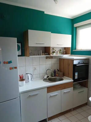 A modern kitchen with white cabinets, a sink, a refrigerator, and a window.