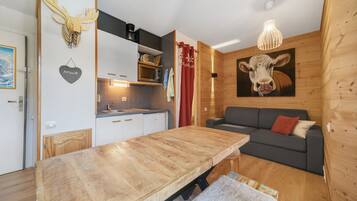A cozy cabin interior with a wooden dining table, a sofa, a kitchen area, and a mounted cow painting.