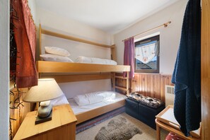 A bunk bed room with a wooden headboard, a bedside table with a lamp, a small stool, and a window with curtains. - Apartment "Au Pieds des Pistes" in Les Esserts with Mountain View, Balcony and Wi-Fi (Morillon)