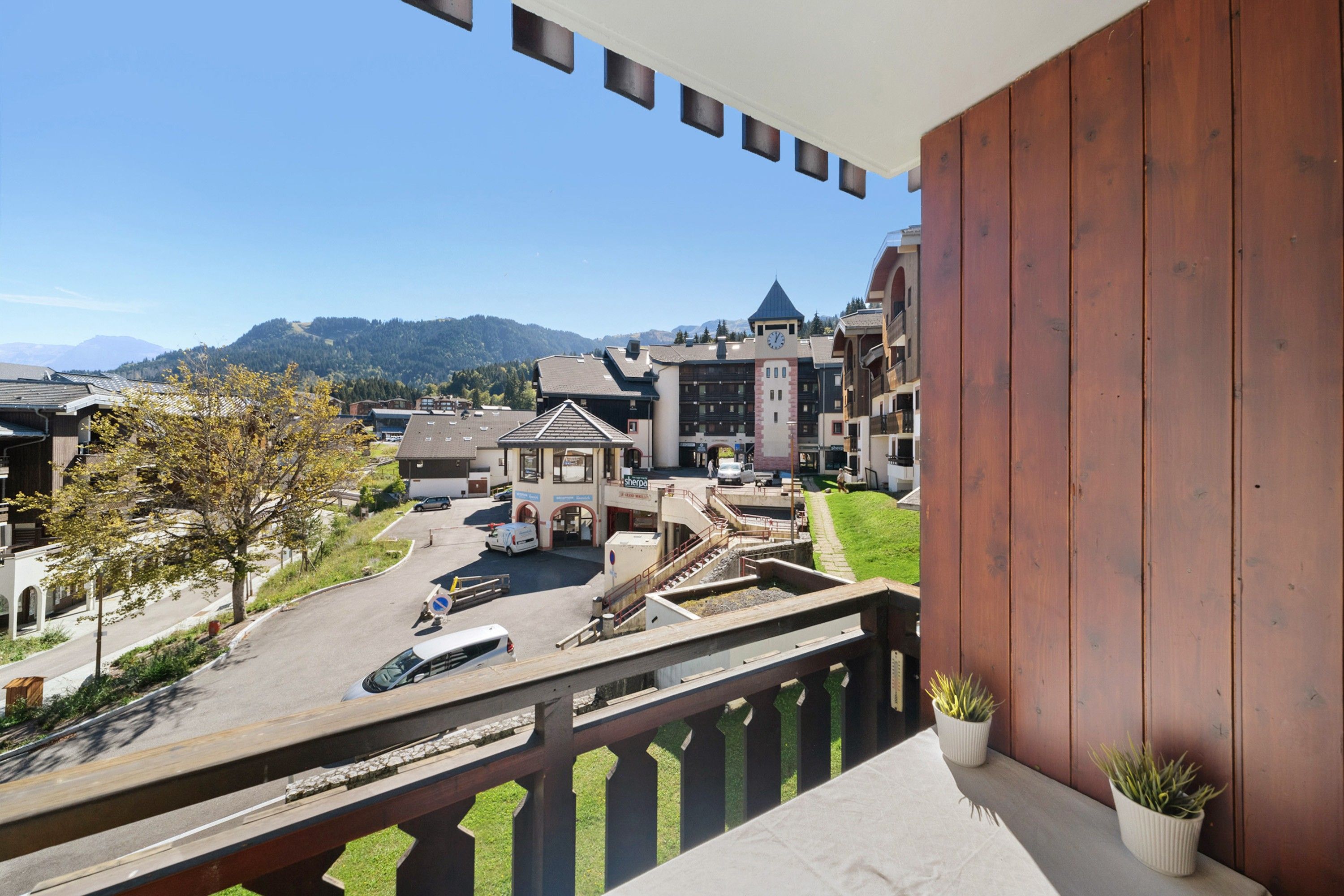 Ein Balkon mit Blick auf eine Stadt, darunter ein Gebäude mit einem Glockenturm, ein Parkplatz und ein Berg im Hintergrund.