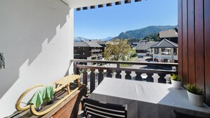 Een balkon met een tafel en stoelen, met uitzicht op een stad met gebouwen en bergen in de verte.