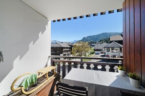A balcony with a table and chairs, overlooking a town with buildings and mountains in the distance. - Apartment "Au Pieds des Pistes" in Les Esserts with Mountain View, Balcony and Wi-Fi (Morillon)